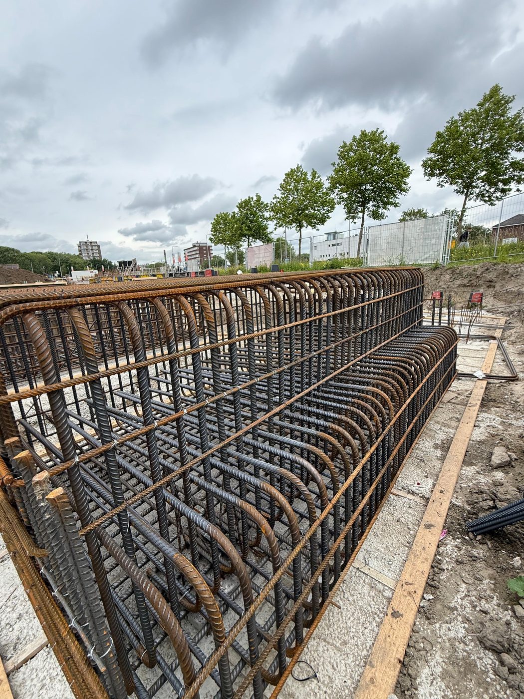 Beugelwapening van een funderingsbalk in de open sleuf, met bomen langs de bouwplaats