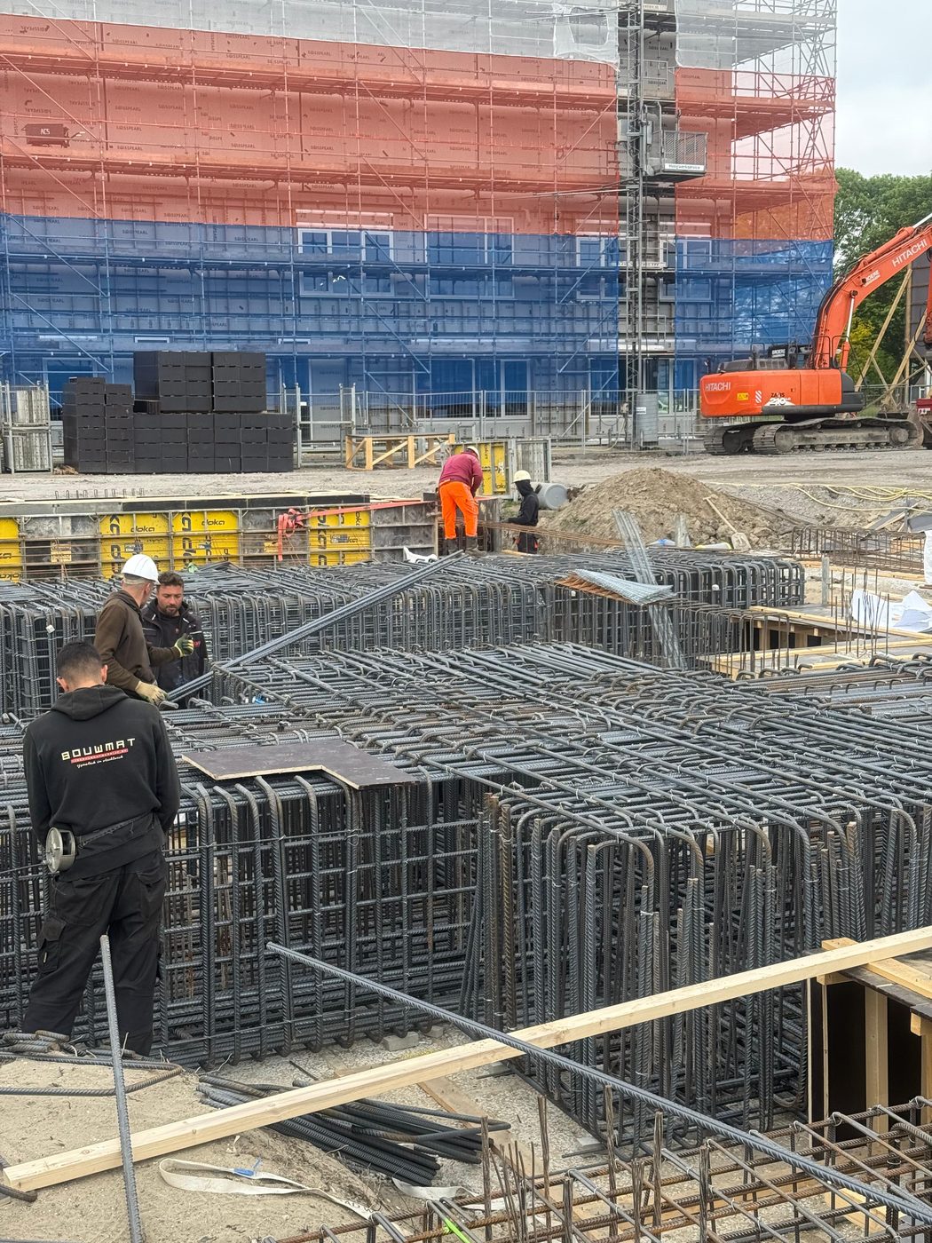 Vlechtwerk aan de fundering, met de hoogbouw in de steigers erachter